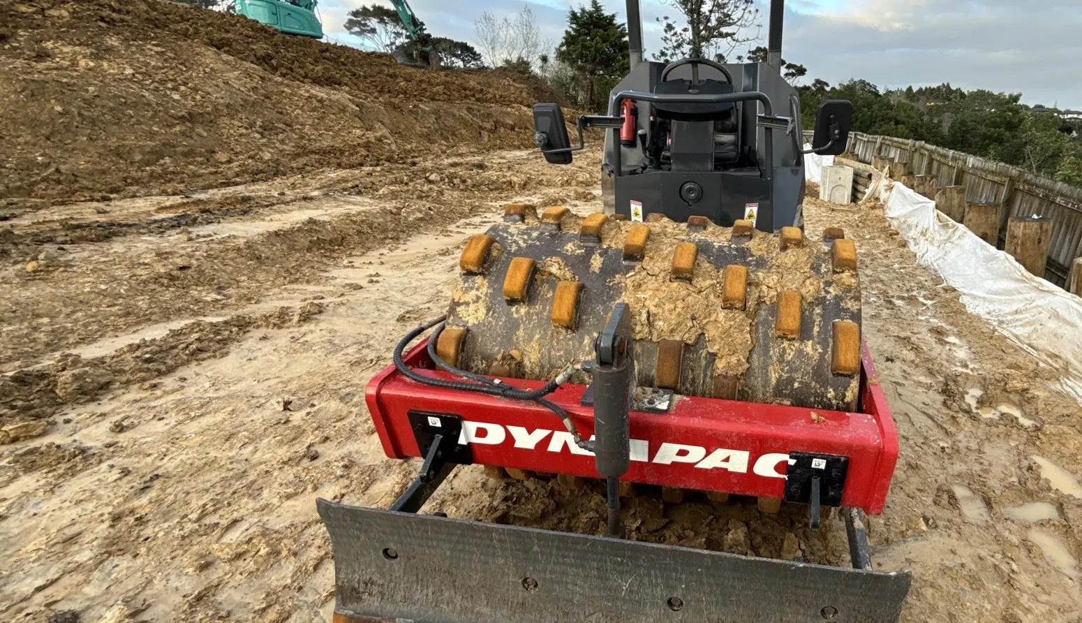 Pad foot roller compacting engineered fill beside a timber retaining wall